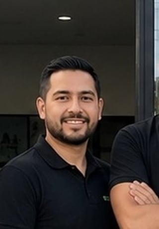 Man with dark hair and beard smiling at camera wearing black polo shirt